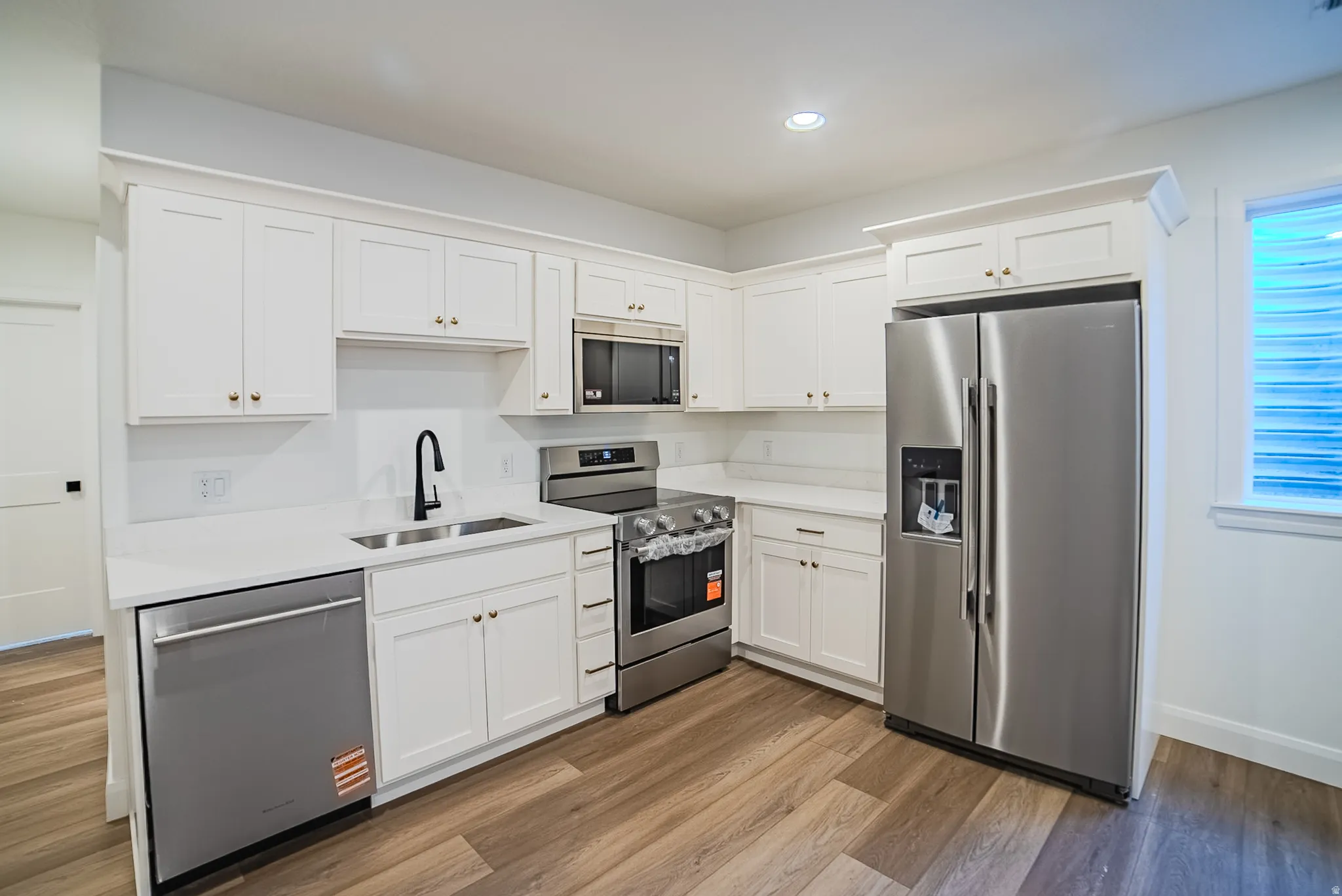 Kitchen featuring white cabinetry, stainless steel appliances, wood-finish flooring, recessed lighting, and a white countertop