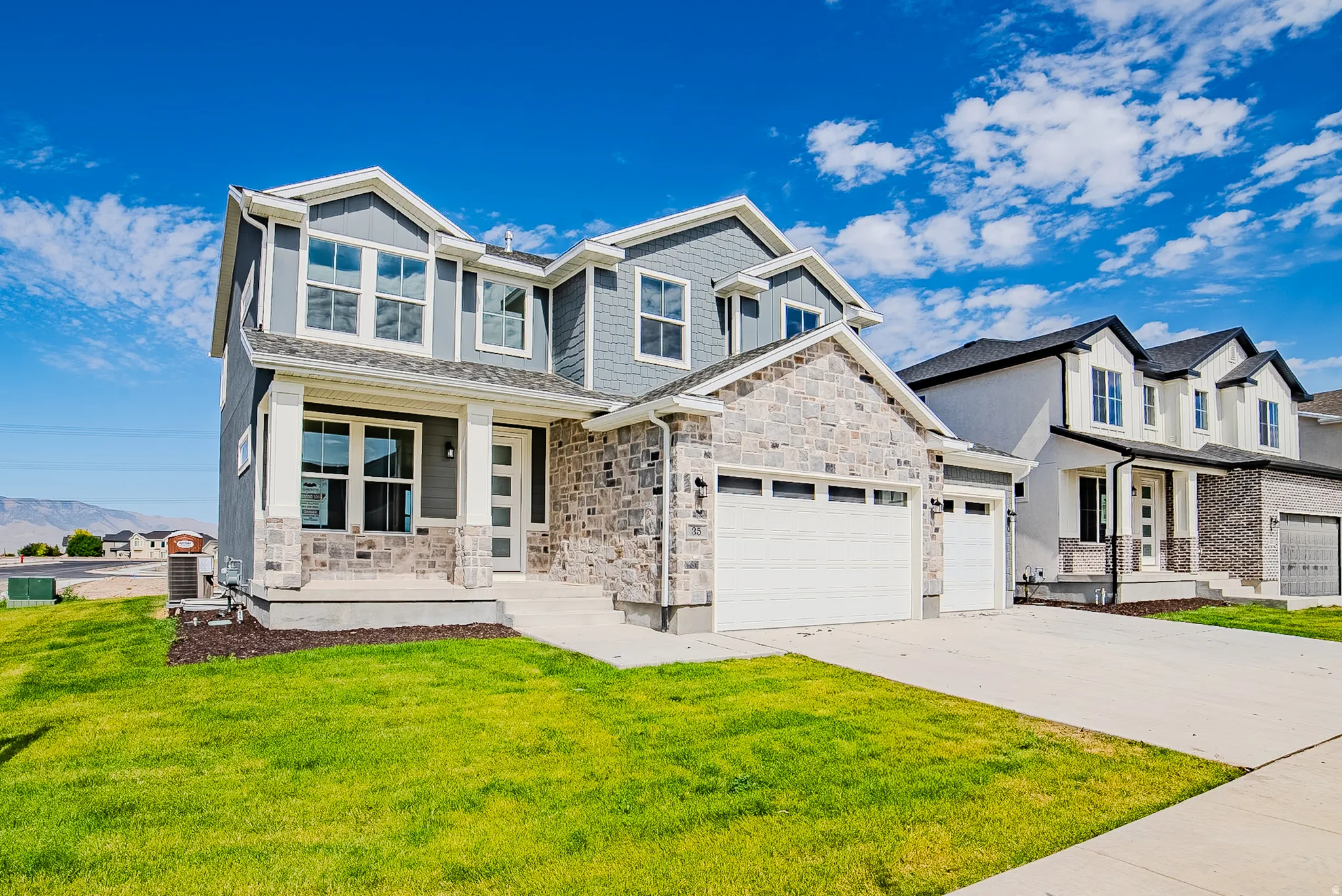 Contemporary two-story residence with a stone and siding facade, a double-door garage, an inviting front porch, and a concrete driveway