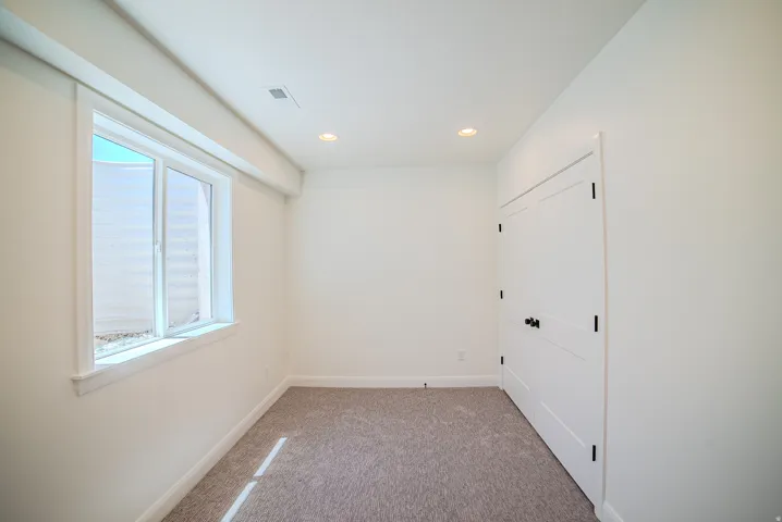Recessed ceiling lighting, white walls, carpet flooring, a window with white trim, and a bi-fold door with black hardware