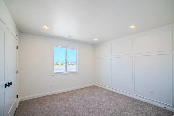 Recessed lighting illuminating the room, white panel molding accent wall, neutral-toned carpeting, and a white interior door with black hardware