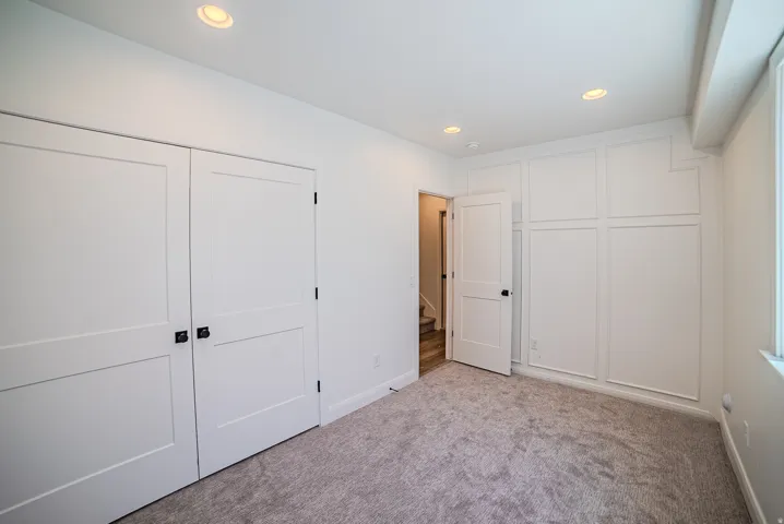 Recessed lighting illuminates the room, featuring a carpeted floor, white walls, and a window providing natural light