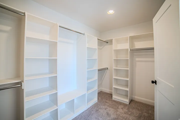 Built-in closet organization system featuring multiple shelving units, hanging rods, recessed lighting, and soft carpet flooring