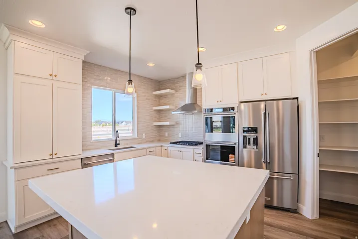 Gourmet kitchen with a large central island, white cabinetry, stainless steel appliances, and a tiled backsplash