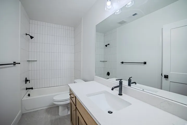 Bathroom featuring a tub/shower combination with vertical subway tile surround, single vanity with integrated sink, matte black fixtures, and a frameless mirror