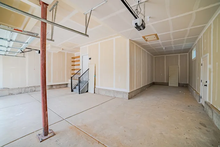 Spacious garage with concrete flooring, built-in wooden shelving, and a black wrought iron staircase