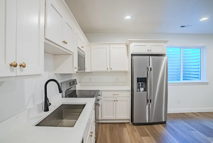 Kitchen featuring white cabinetry with gold-tone hardware, stainless steel appliances, a deep single-basin sink with a matte black faucet, and light-toned wood-finish flooring