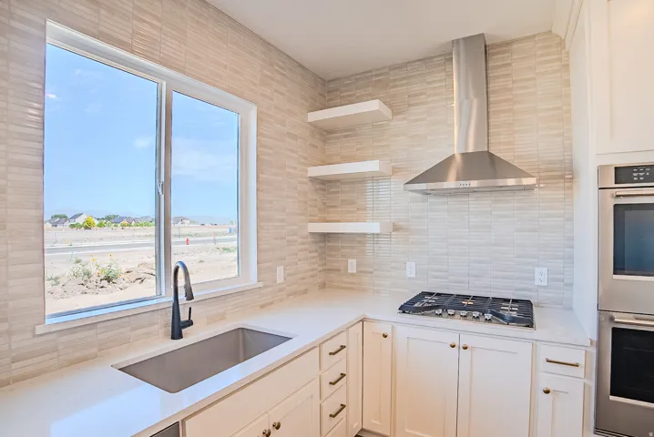 Modern kitchen featuring white cabinetry with brass hardware, a stainless steel range hood, gas cooktop, and integrated wall-mounted double ovens