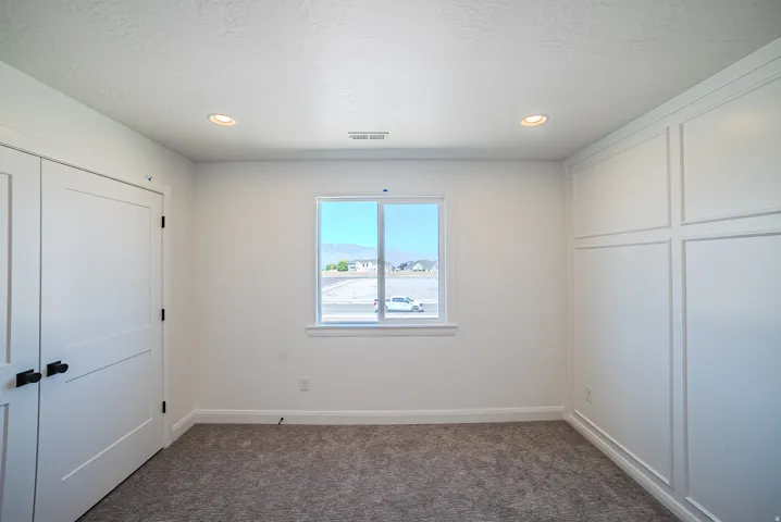 White interior walls, recessed ceiling lighting, a window with exterior scenery, paneled bifold doors with black hardware, and an accent wall featuring wainscoting
