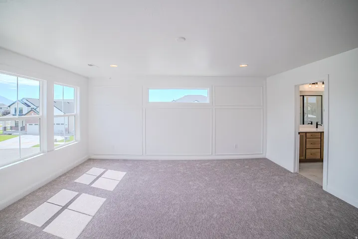 Recessed lighting, light gray carpet, multiple large windows, decorative wall molding, and an open doorway to a bathroom