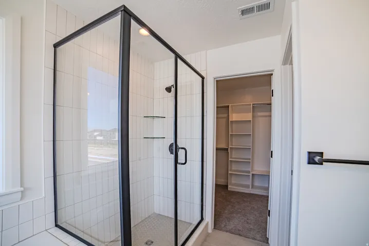 Glass-enclosed shower with black trim, vertical subway tile surround, and built-in glass shelving
