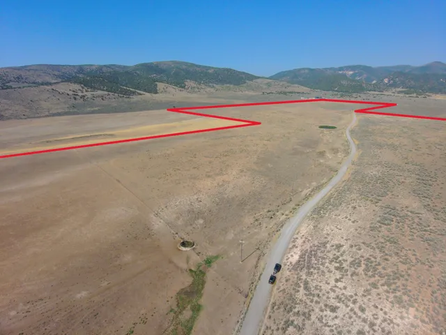 Expansive open land featuring natural vegetation, a winding unpaved road, and distant mountainous terrain