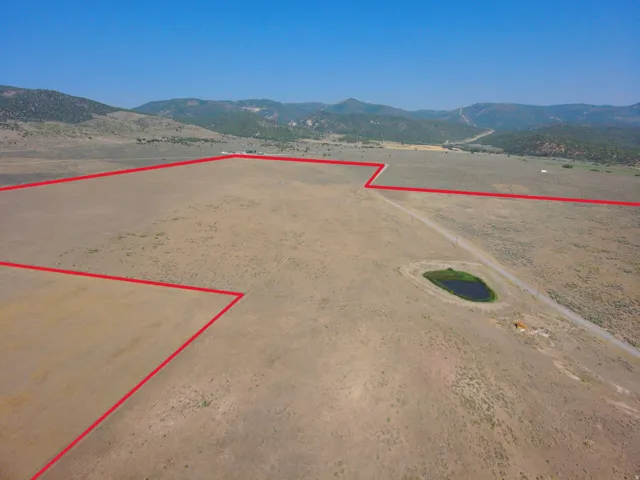 Expansive land parcel featuring a natural pond, unpaved access road, and mountainous backdrop
