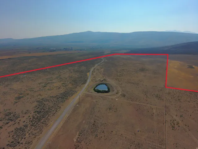Expansive undeveloped land featuring a paved road, a natural pond, and a distant mountain backdrop
