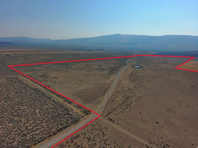 Expansive land parcel with a natural pond, unpaved road access, and distant mountain scenery