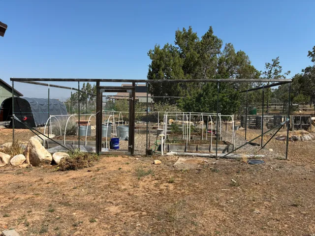 Fenced garden area featuring raised beds, a greenhouse structures
