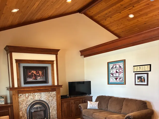 Wood-finish flooring, vaulted wood-paneled ceiling with recessed lighting, stone-clad fireplace with an ornate iron insert, and wood mantel