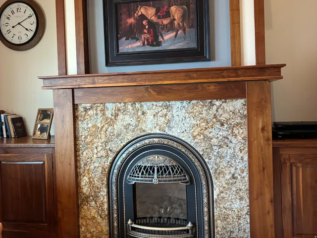 Wood mantelpiece with decorative trim, stone surround fireplace with an ornate cast iron insert, and a black stone hearth