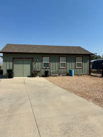 Professional Woodworking Shop with overhead door, vertical siding, a shingled roof, three windows, and a concrete driveway