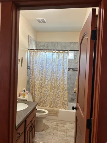 Bathroom featuring a wood-finish vanity with an integrated sink, tiled flooring, and a tiled shower surround