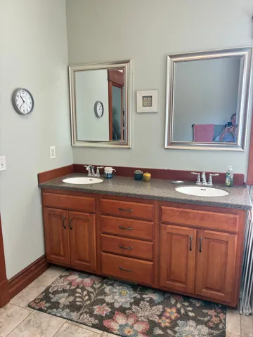 Double vanity with warm-toned cabinetry, dual undermount sinks, and granite countertop