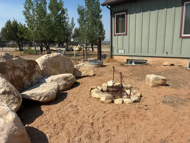 Exterior featuring board and batten siding, rock-lined fire pit, and mature trees