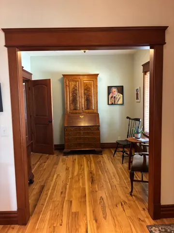 Hardwood flooring throughout, wide framed doorway with substantial trim, solid wood paneled door, and wood baseboards