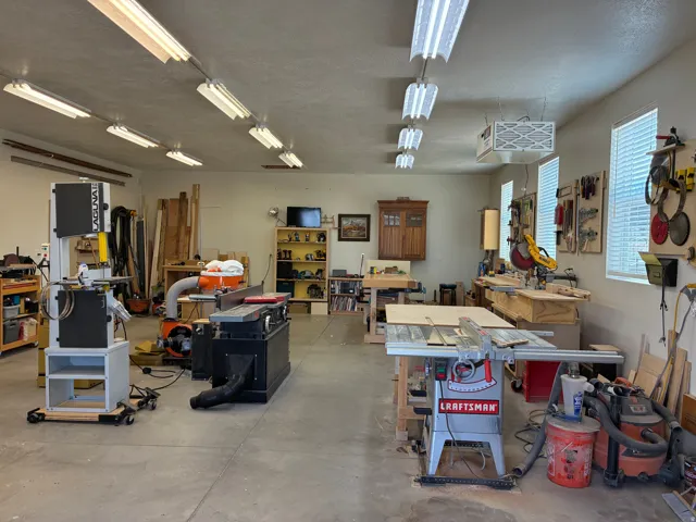 Spacious workshop featuring abundant fluorescent ceiling lighting, concrete flooring, multiple windows, and built-in shelving