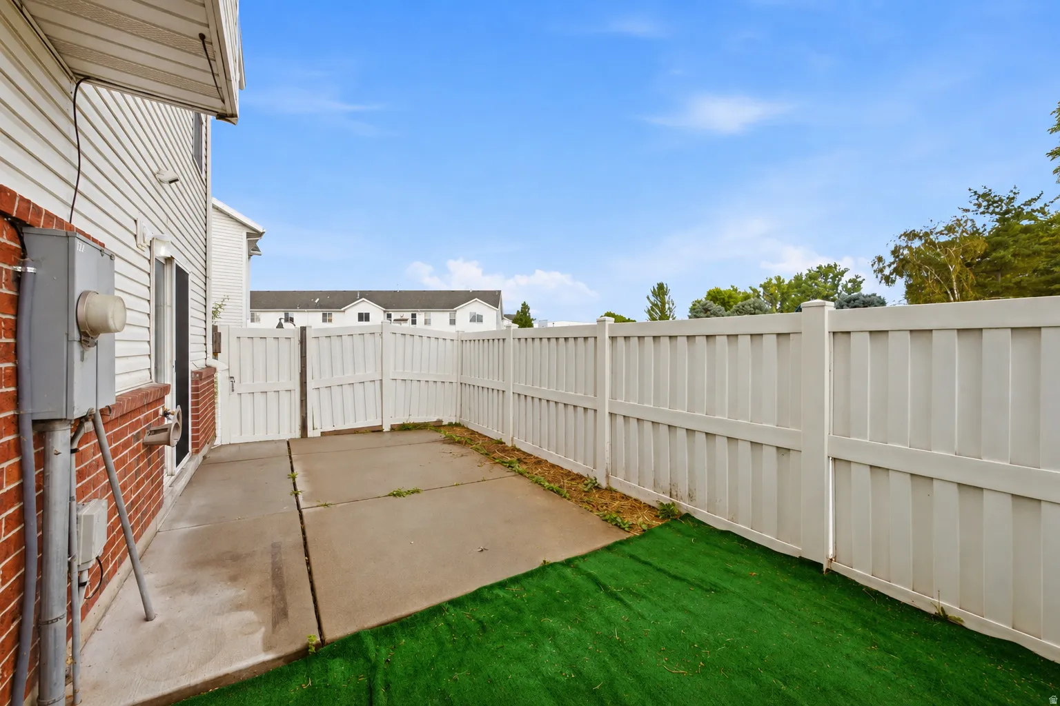 Enclosed outdoor space featuring a concrete patio, artificial turf, and privacy fencing