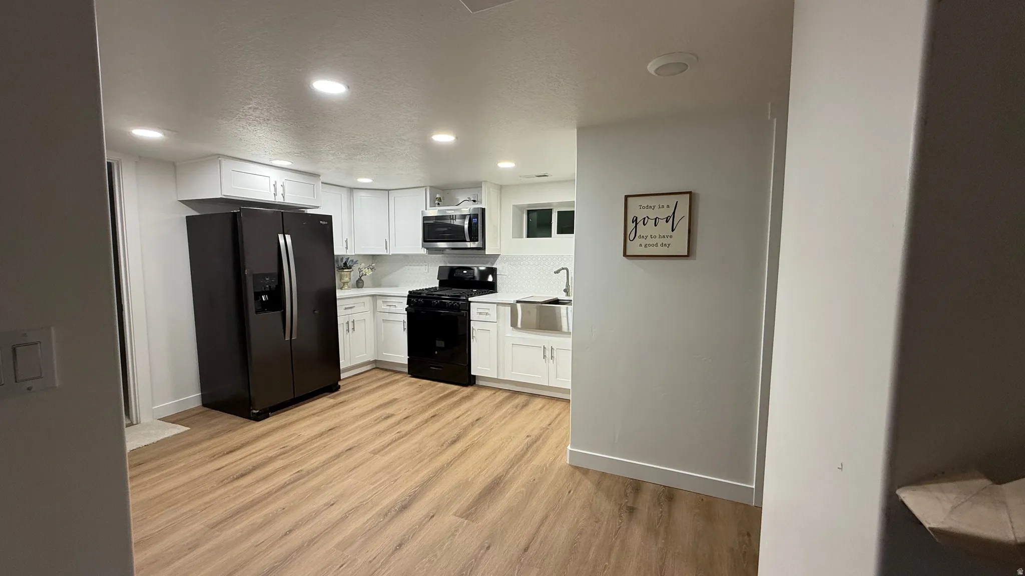 Kitchen featuring light wood-finish flooring, white cabinetry, recessed lighting, and black appliances