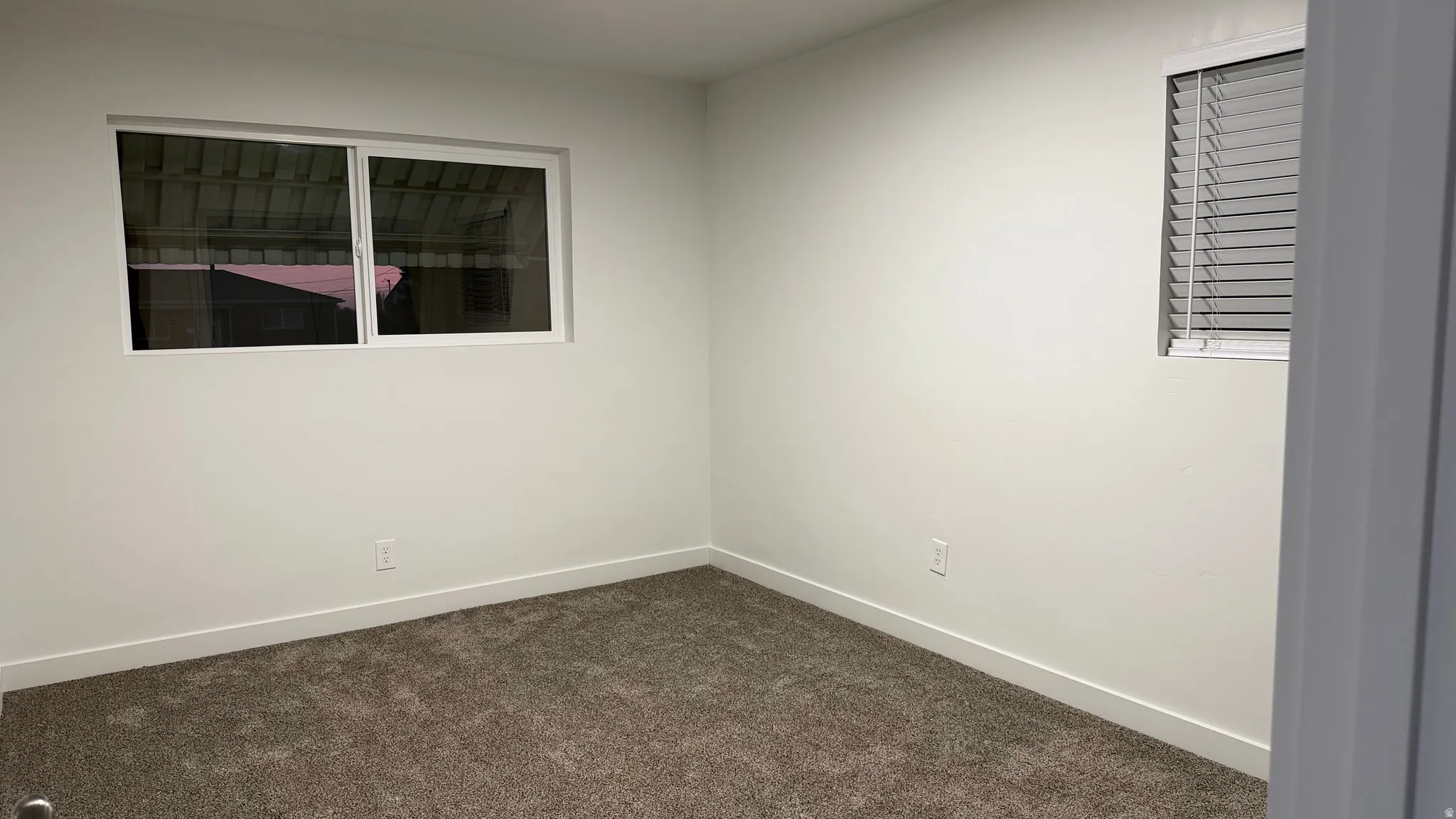 Spacious bedroom with neutral wall finishes, carpet flooring, and abundant natural light from dual windows