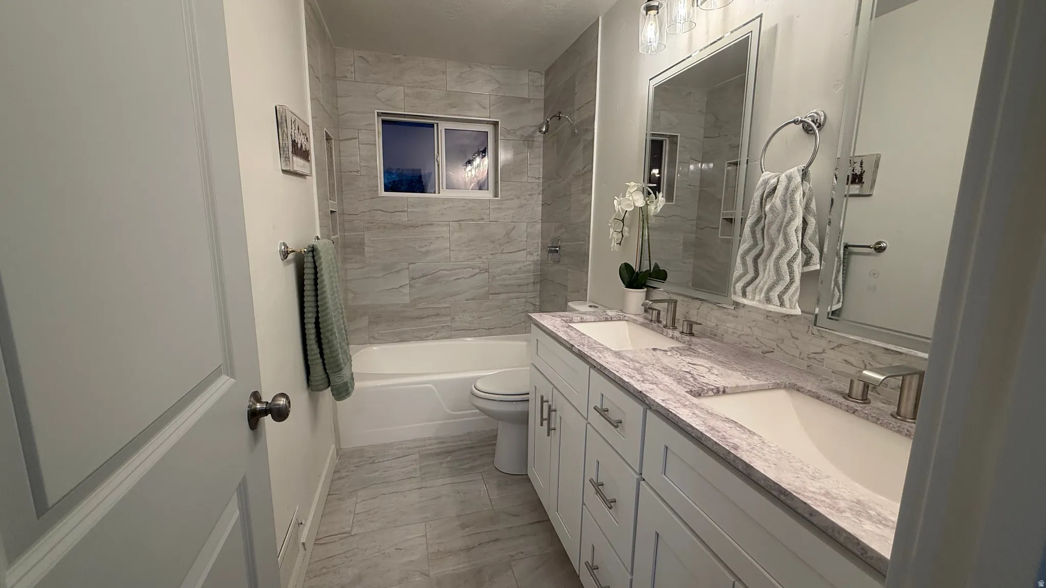 Bathroom featuring a dual vanity with undermount sinks, a bathtub with tiled surround, a tiled floor, and a window