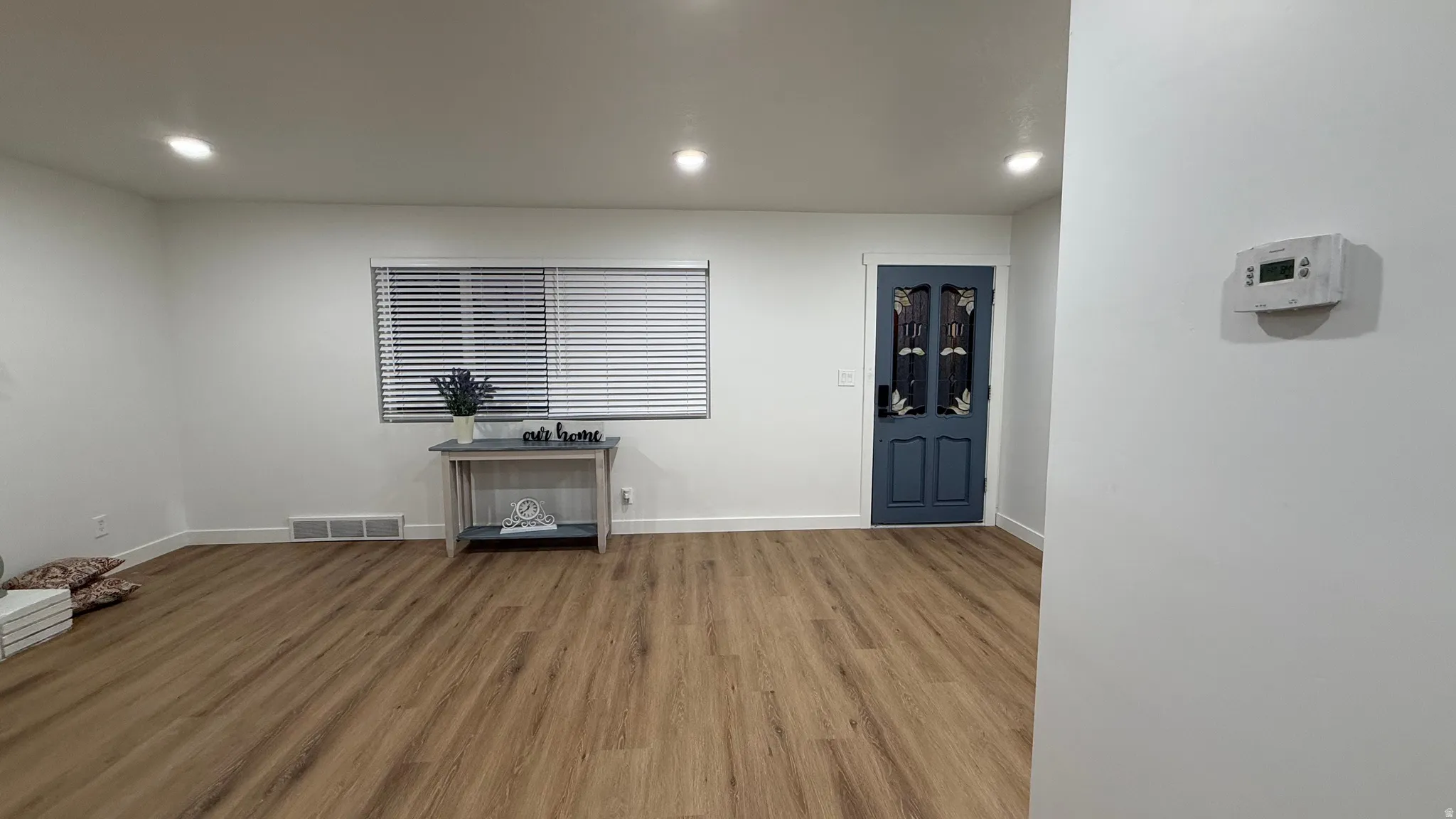 Spacious interior with wood-finish flooring throughout, recessed ceiling lighting, and large window with horizontal blinds