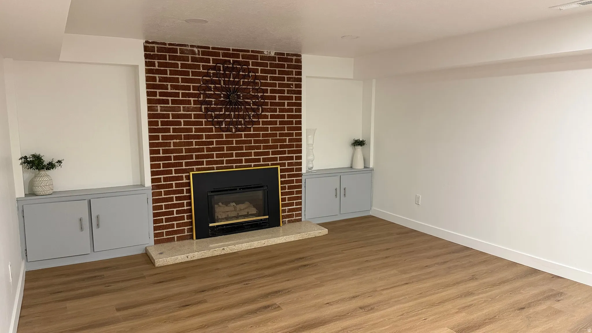 Brick-clad fireplace with a black and gold-toned insert, built-in cabinetry, recessed wall niches, and wood-finish flooring