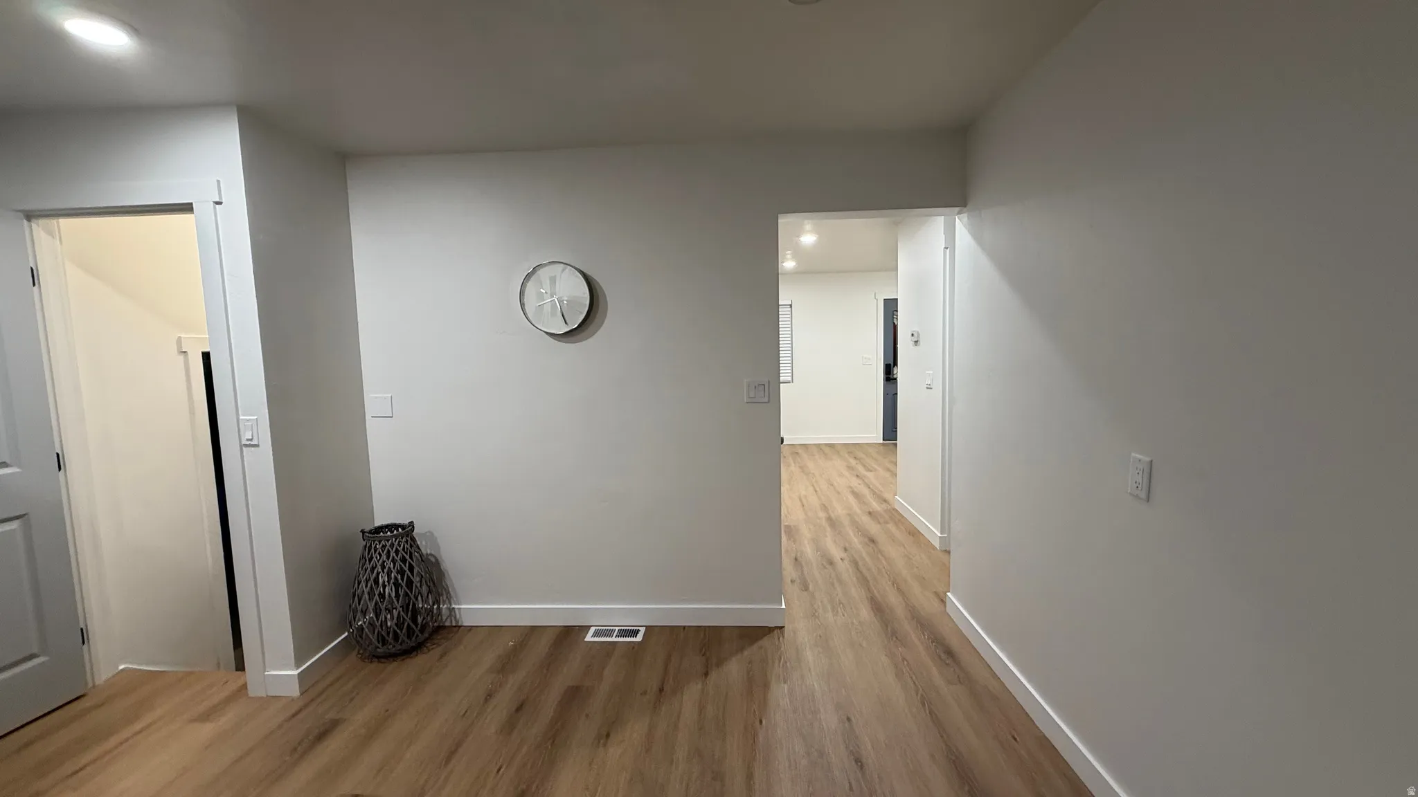 Bright hallway showcasing warm wood-finish flooring, fresh white walls, and recessed lighting throughout