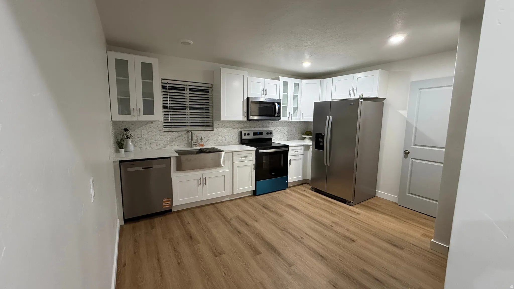 White cabinetry, stainless steel appliances, wood-finish flooring, white countertops, and a farmhouse sink