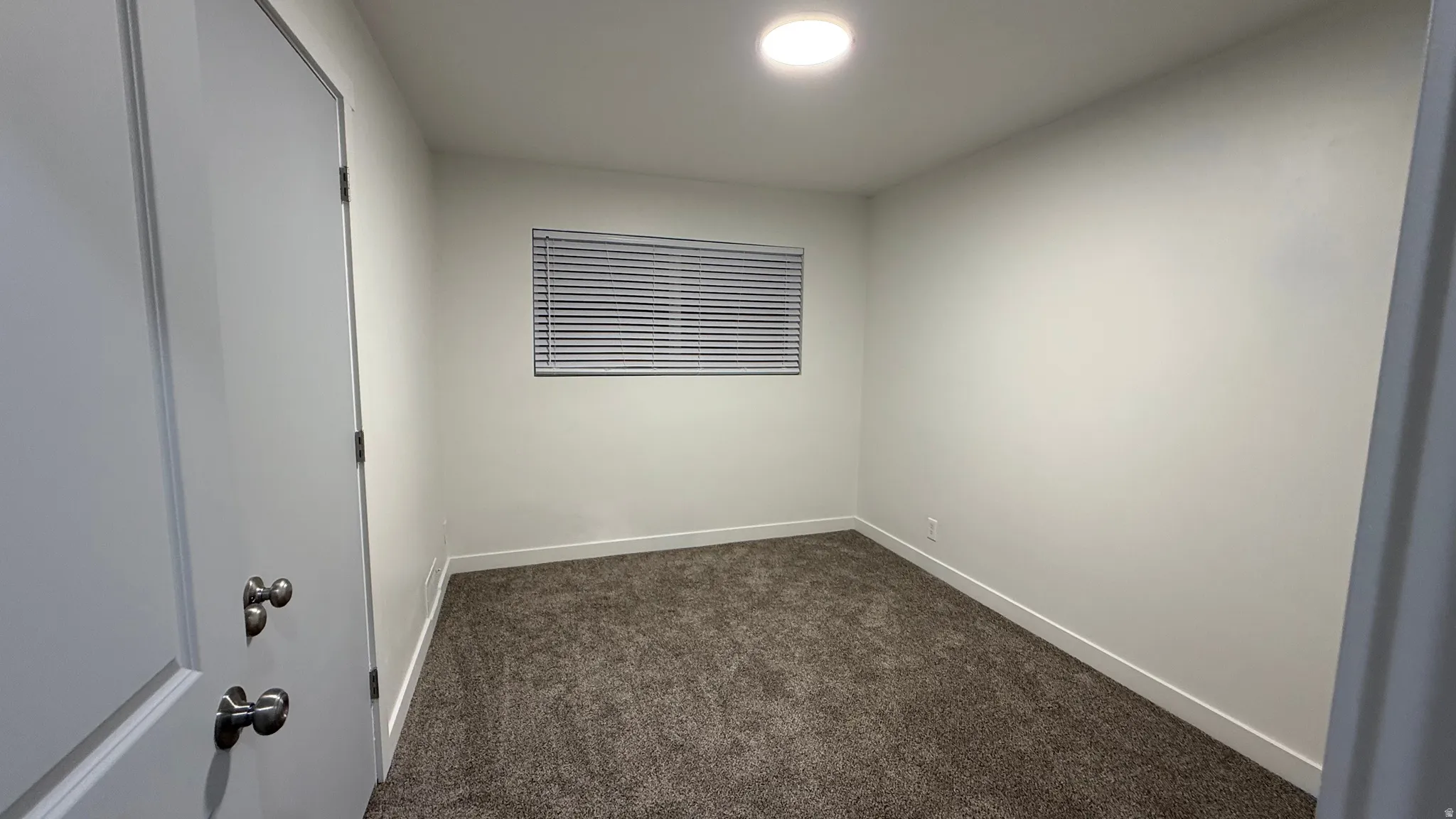 Recessed ceiling light, neutral wall paint, window with blinds, and textured carpet flooring