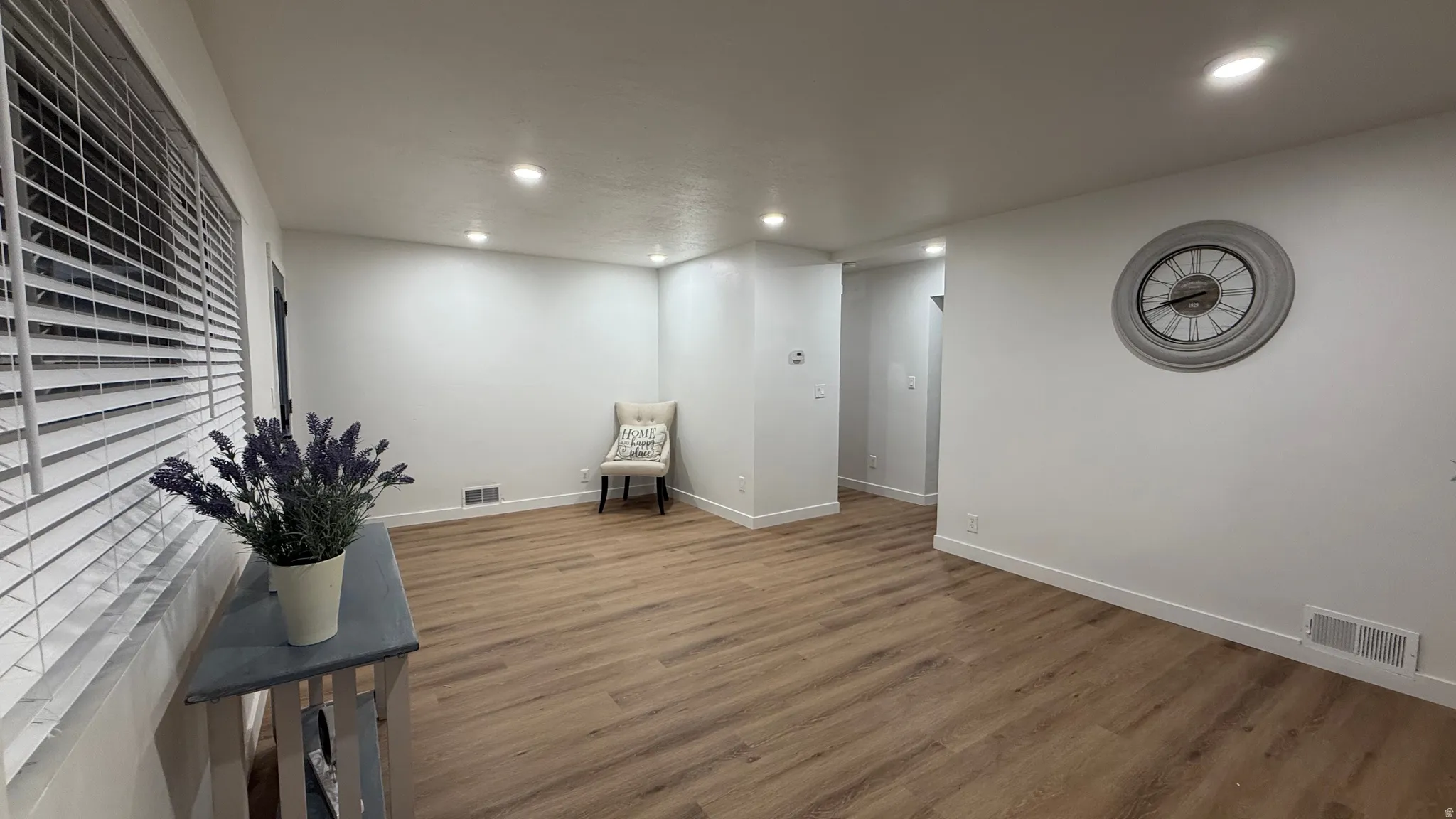 Bright, open living space featuring warm wood-finish flooring throughout, recessed ceiling lighting, and clean white walls