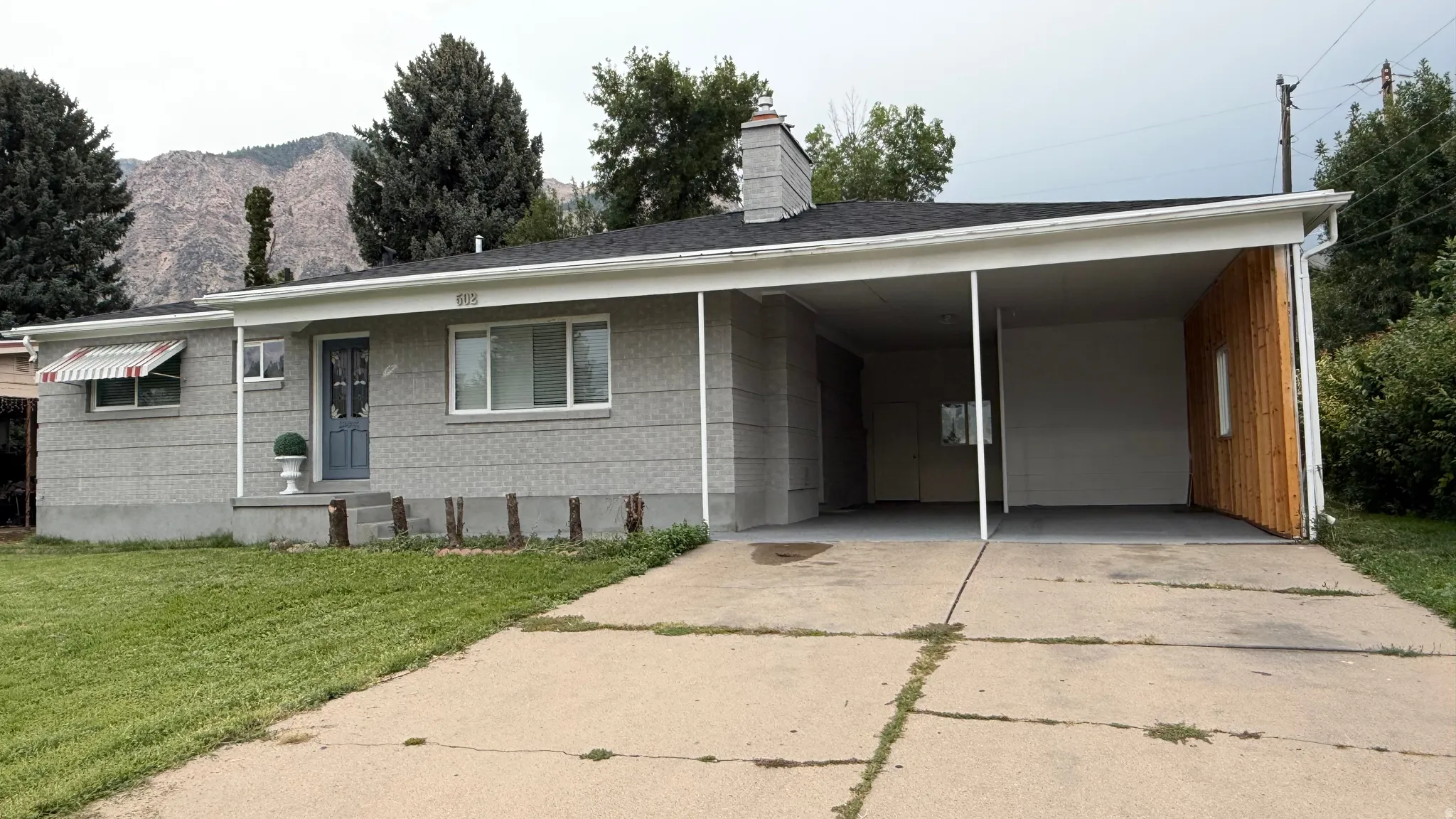Mid-century modern ranch home featuring a clean-lined facade with horizontal siding, carport with wood-finish accent paneling, and expansive concrete driveway