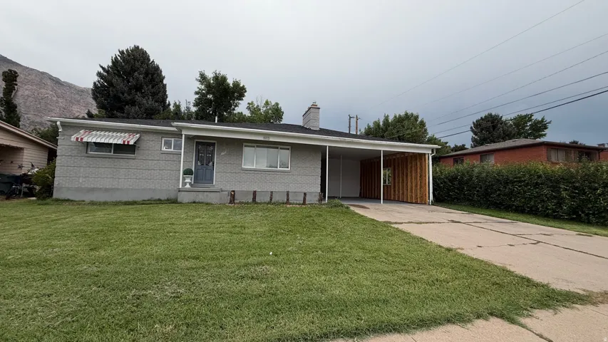 Charming mid-century residence featuring a brick exterior, carport with wood-finish garage door, and expansive front lawn with mature landscaping