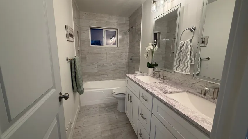 Bathroom featuring a dual vanity with undermount sinks, a bathtub with tiled surround, a tiled floor, and a window