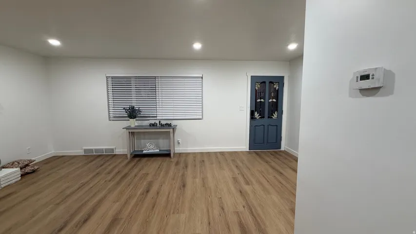 Spacious interior with wood-finish flooring throughout, recessed ceiling lighting, and large window with horizontal blinds