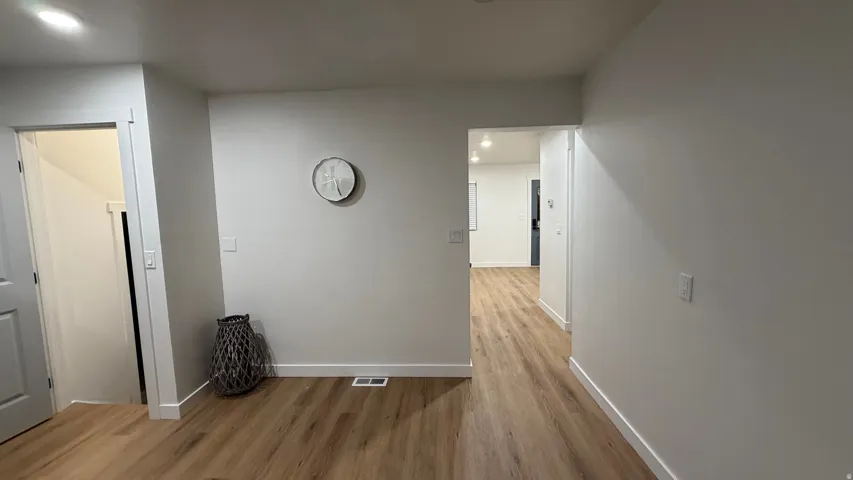 Bright hallway showcasing warm wood-finish flooring, fresh white walls, and recessed lighting throughout