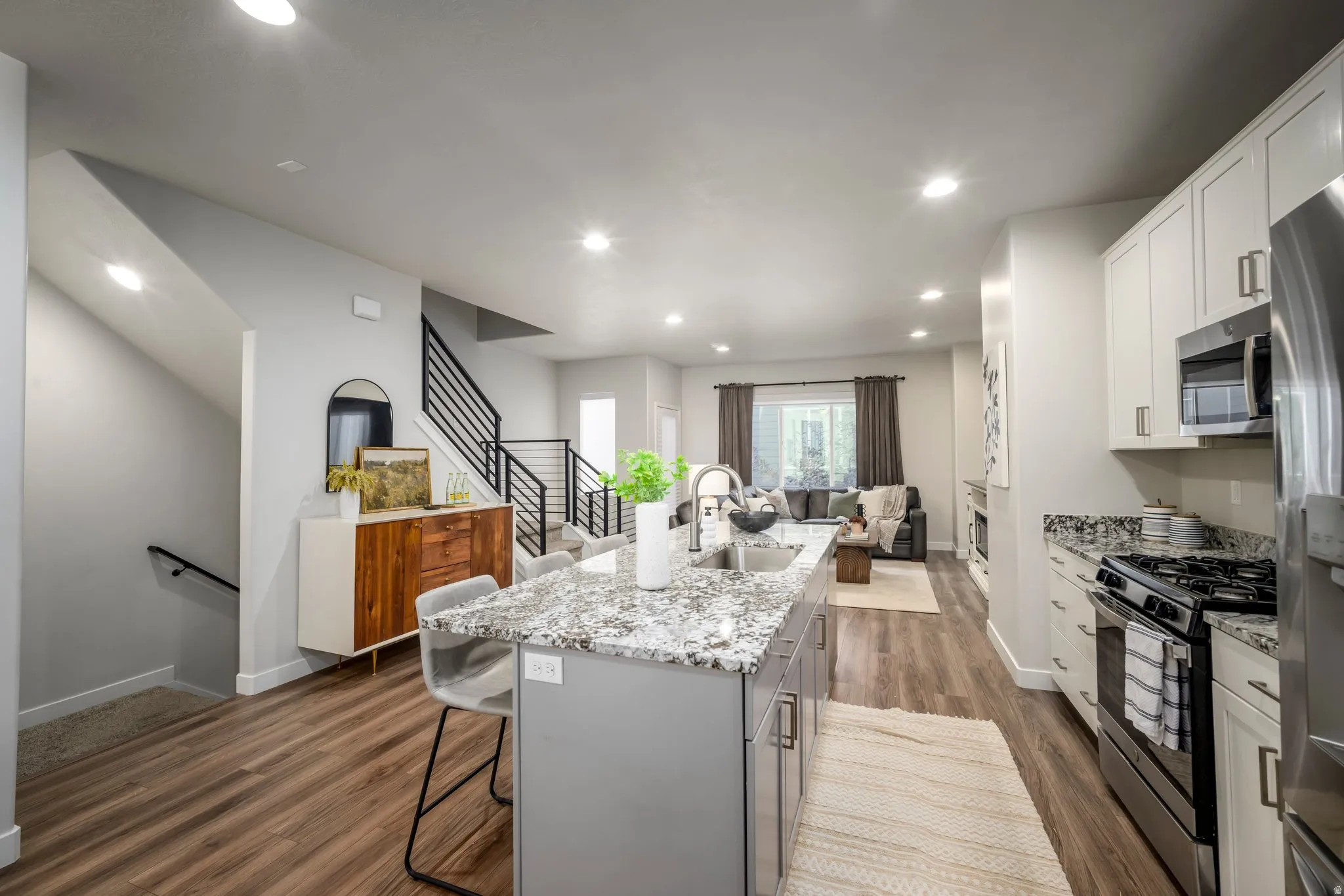 Open-concept kitchen and living area featuring a large granite-topped island with seating, stainless steel appliances, white cabinetry, and wood-finish flooring throughout