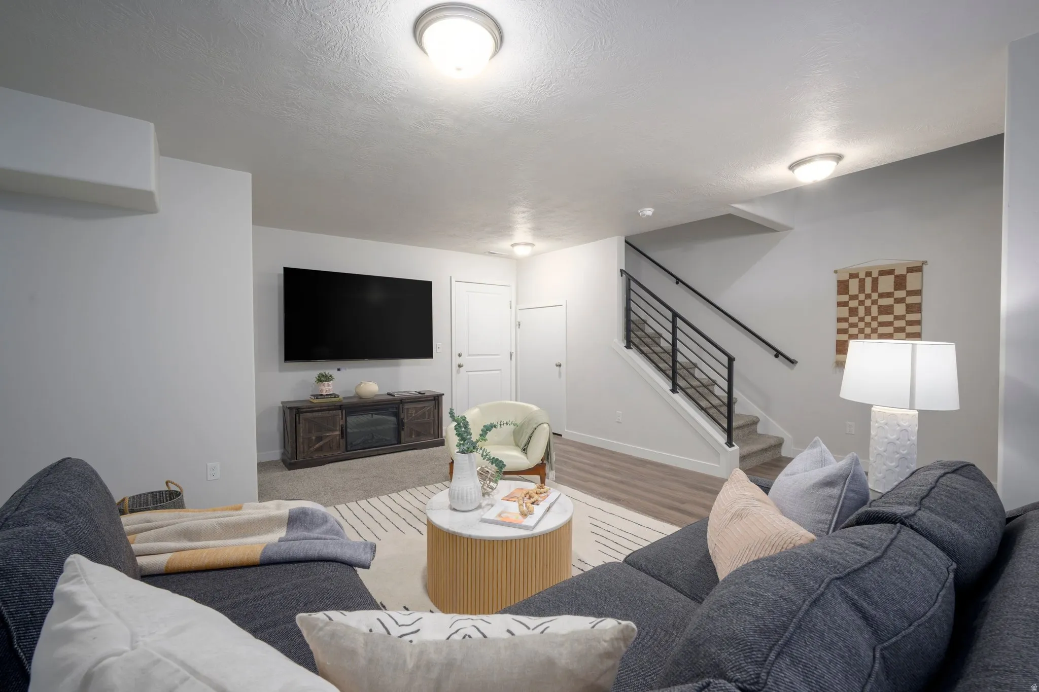 Modern lower-level recreation room featuring plush sectional seating, wood-finish flooring throughout, and a media wall with flat-screen television mounted above built-in cabinetry