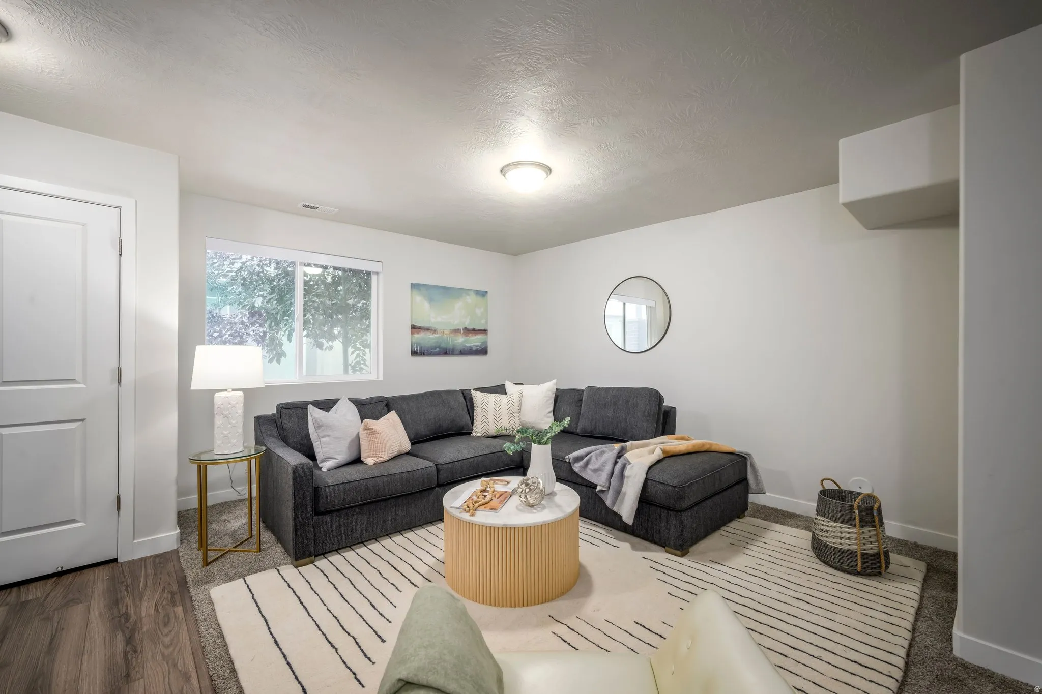 Finished basement recreation room featuring a dark upholstered sectional sofa, wood-finish flooring with geometric area rug, recessed ceiling lighting, and large windows allowing natural light