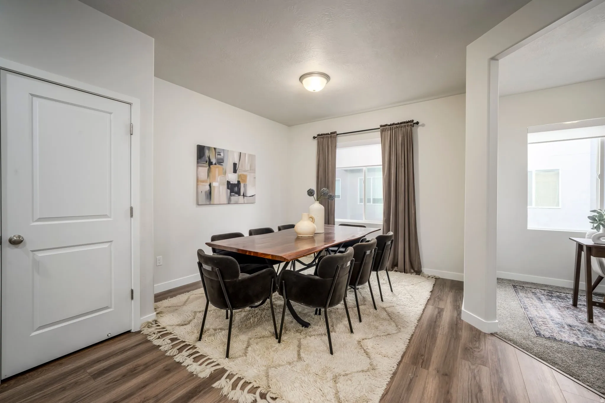 Bright dining area featuring a wood-finish plank floor, neutral wall finishes, and abundant natural light from multiple windows dressed with neutral drapery