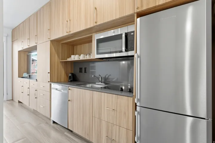Integrated stainless steel appliances, extensive wood-finish cabinetry, built-in microwave, compact dishwasher, and a durable countertop with an undermount sink