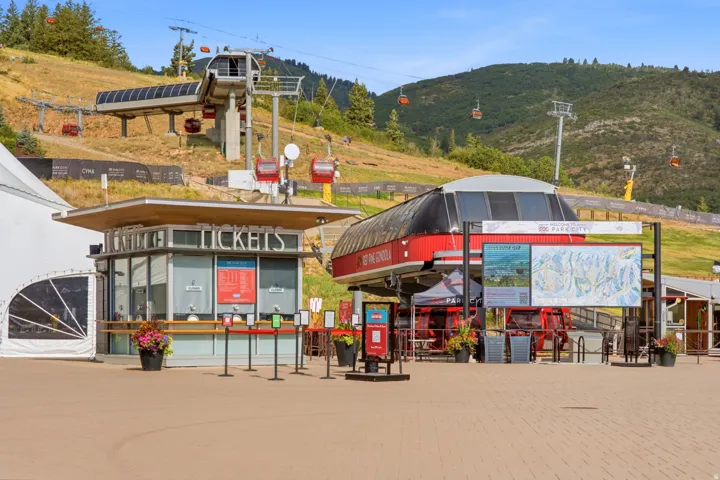 Gondola station with a ticket booth, paved plaza, and mountain backdrop