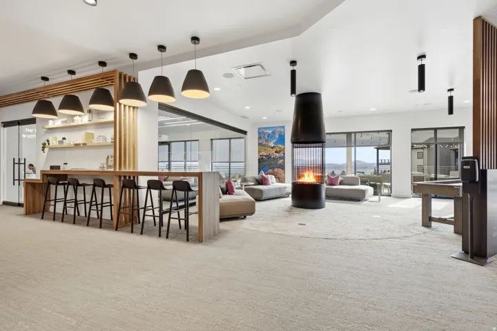 Open-concept common area featuring a built-in bar with pendant lighting, a central cylindrical fireplace, and expansive windows