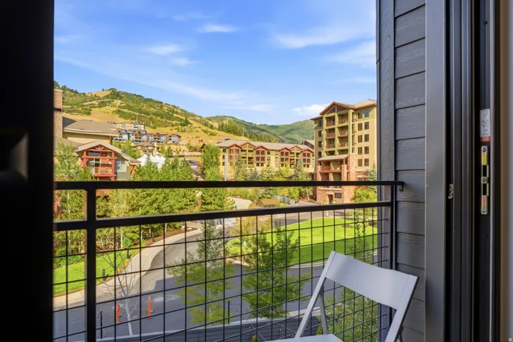 Balcony with black metal railing, offering a mountain backdrop, surrounding greenery, and residential structures